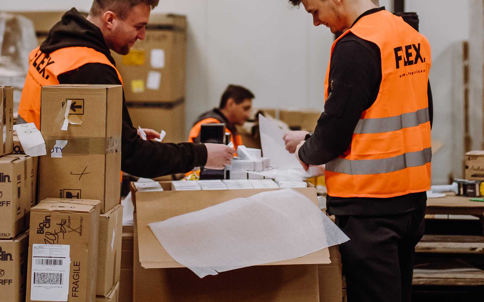 2 Men, wearing Flex vest packing a parcel