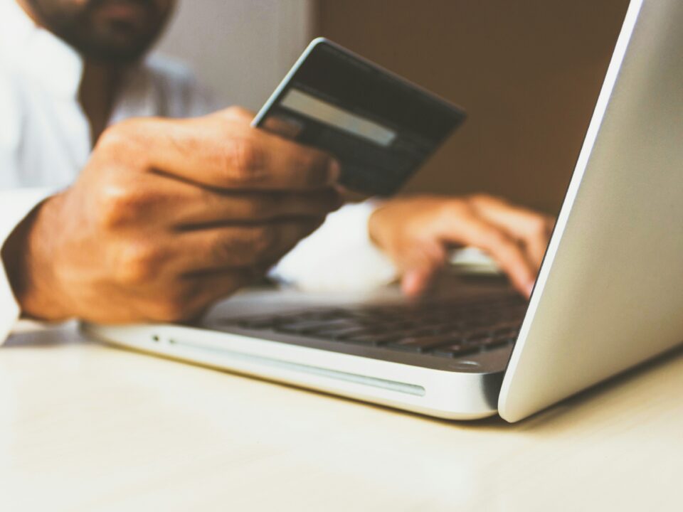 A person uses a laptop while holding a credit card, suggesting online shopping or payment. The scene conveys convenience and modern technology.