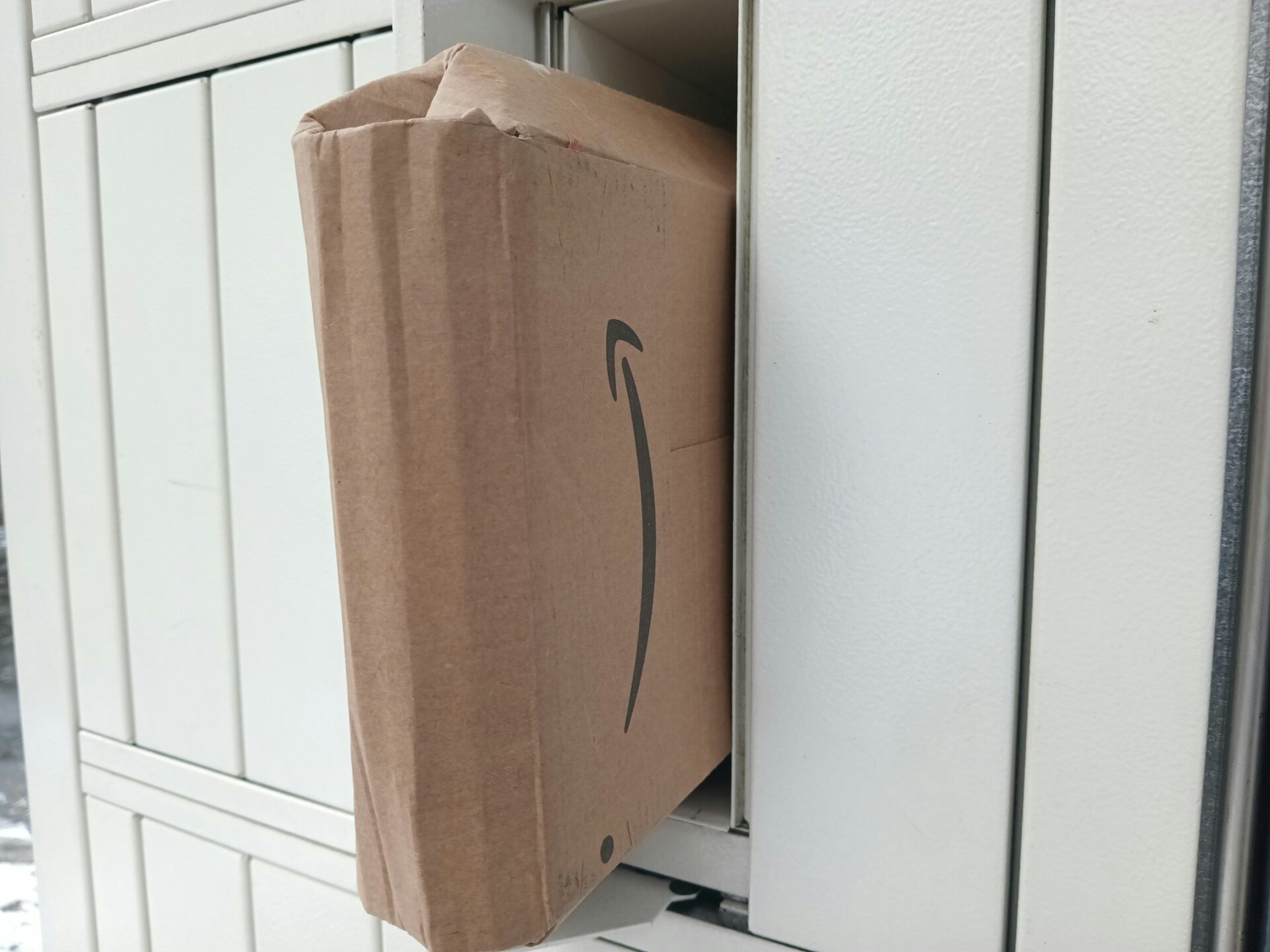 A cardboard package is jammed in a locker, with its corner sticking out. The box displays a partial logo, conveying an unintended delivery issue.