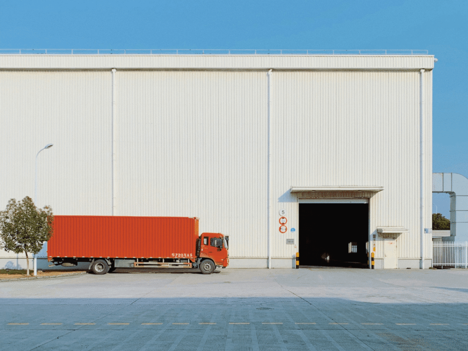 A red freight truck parked at the loading bay of a large warehouse, illustrating logistics in European e-commerce.