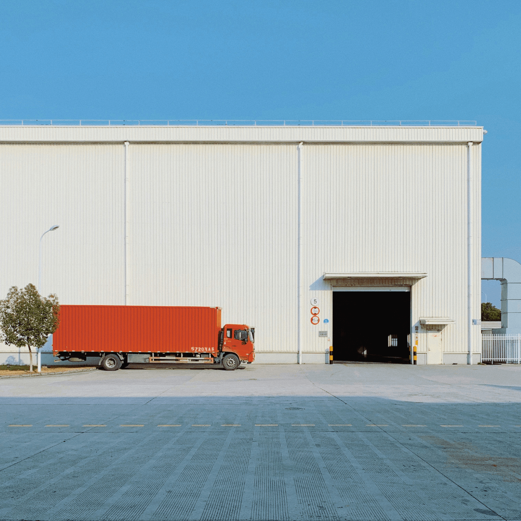 A red freight truck parked at the loading bay of a large warehouse, illustrating logistics in European e-commerce.