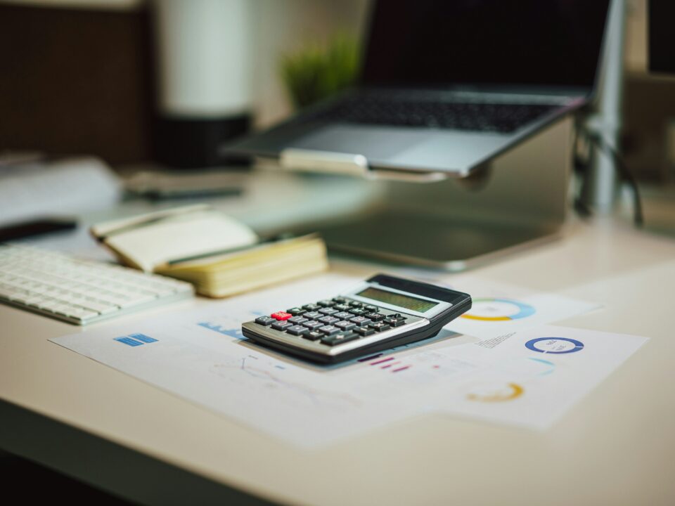 Calculator and documents on a modern office desk with a laptop and keyboard.