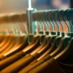 A row of identical black clothing hangers holding dark-colored shirts, arranged neatly on a metal rack in warm store lighting.