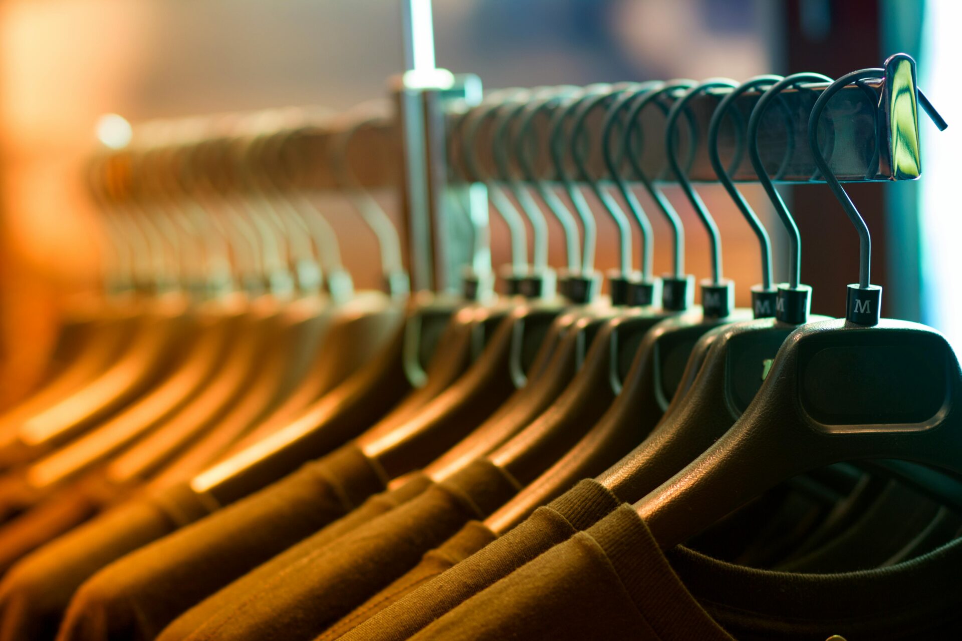 A row of identical black clothing hangers holding dark-colored shirts, arranged neatly on a metal rack in warm store lighting.
