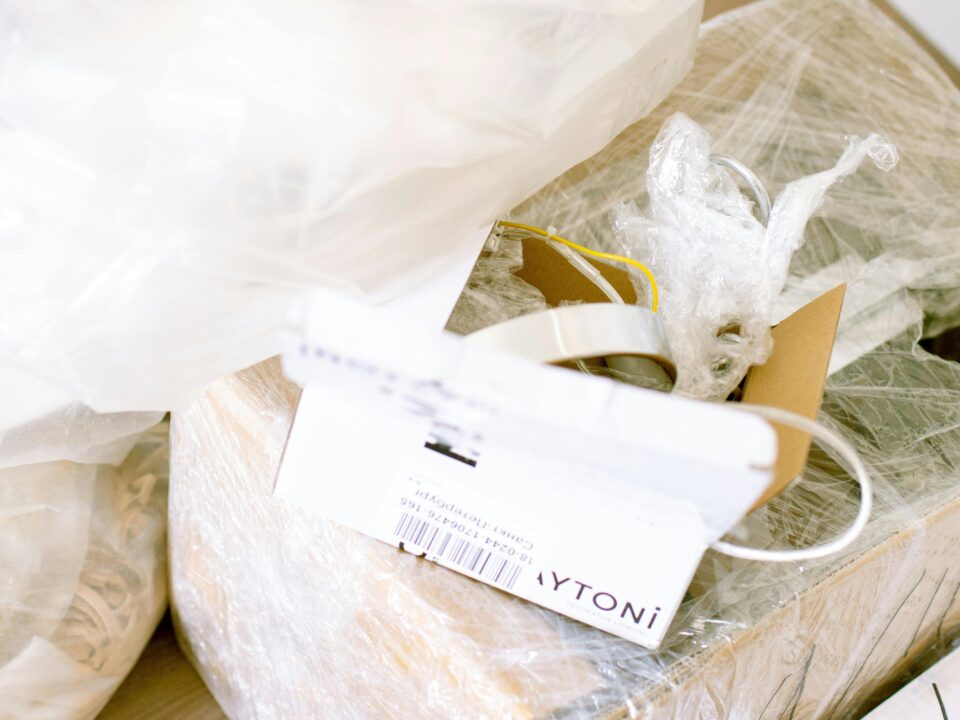 A cardboard shipping box wrapped in shrink wrap, partially opened to show lighting fixture parts and packing materials.