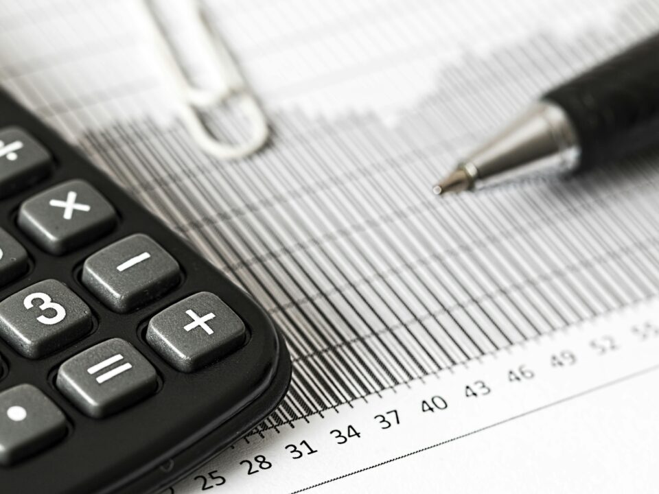 A close-up of a calculator and a pen resting on a printed financial chart with numbers and grid lines.
