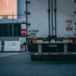 Rear view of a large truck with brake lights on at an industrial facility gate.