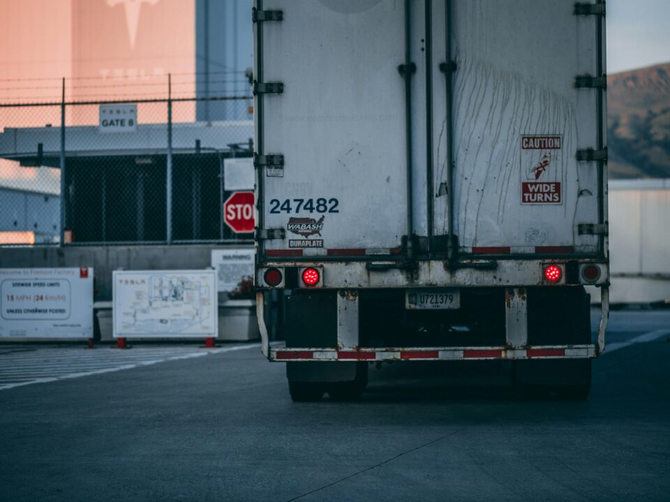 Rear view of a large truck with brake lights on at an industrial facility gate.