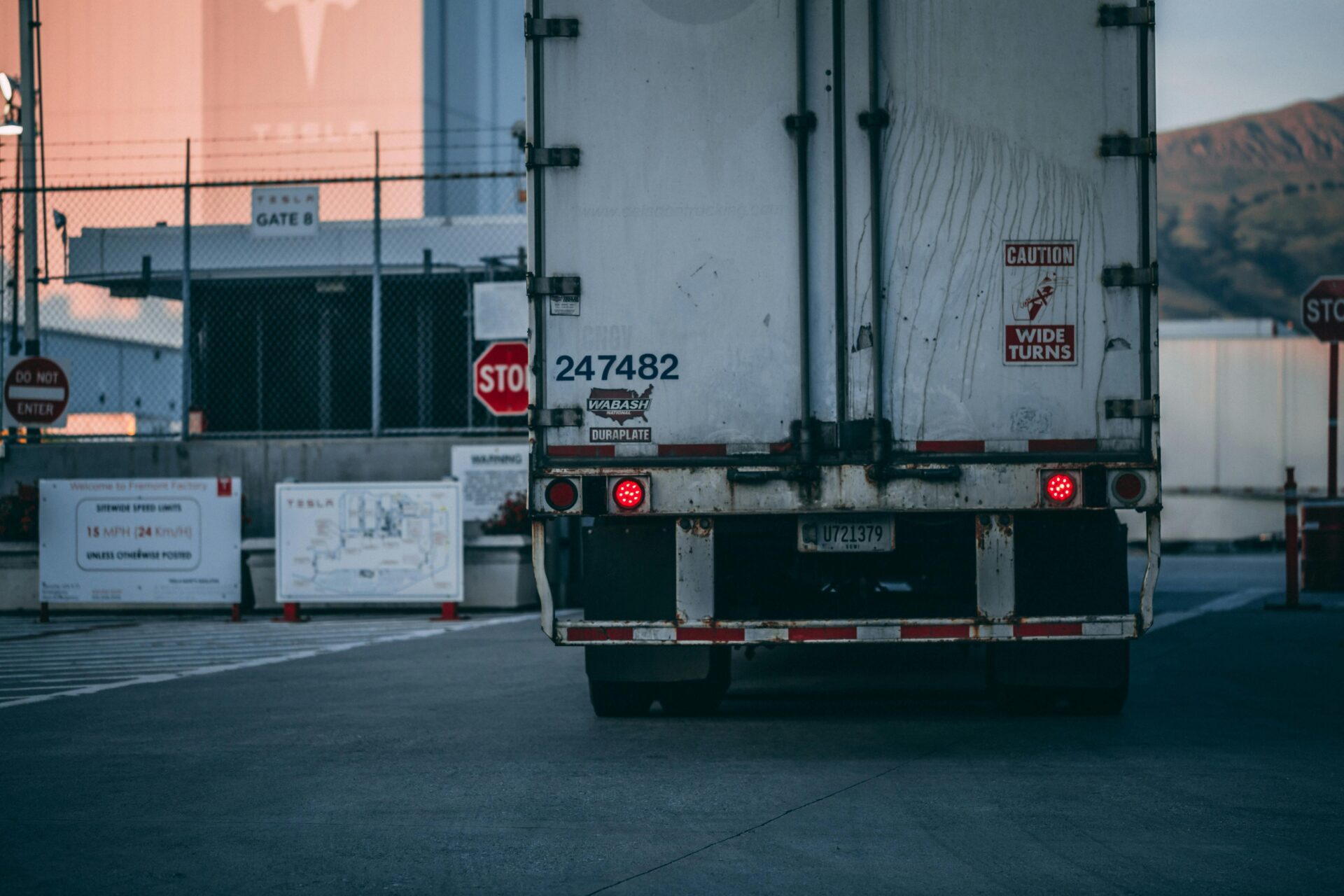 Rear view of a large truck with brake lights on at an industrial facility gate.