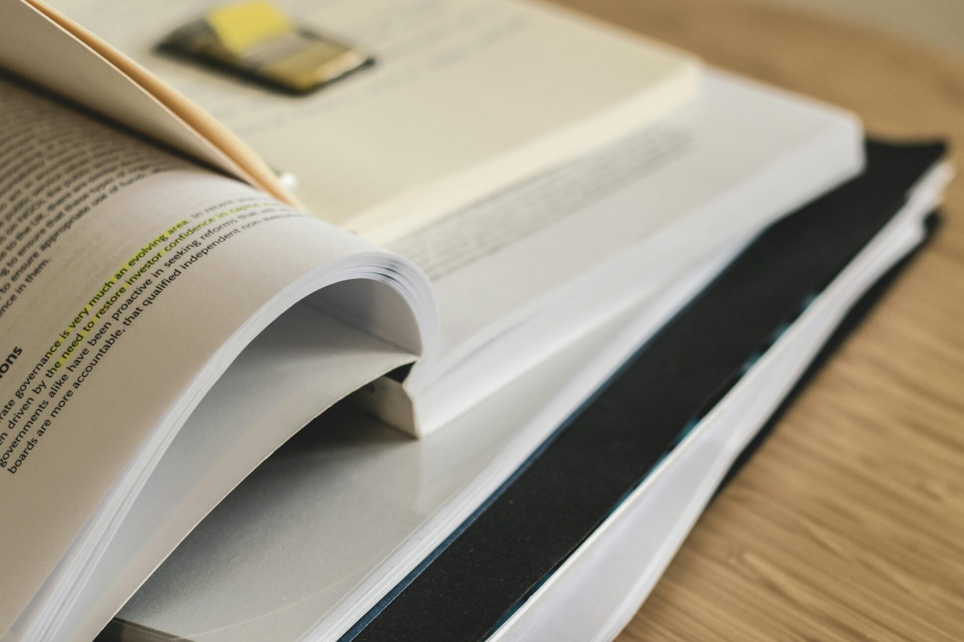 A stack of open books with text highlighted in yellow sits on a wooden surface. The scene conveys study, research, and learning.