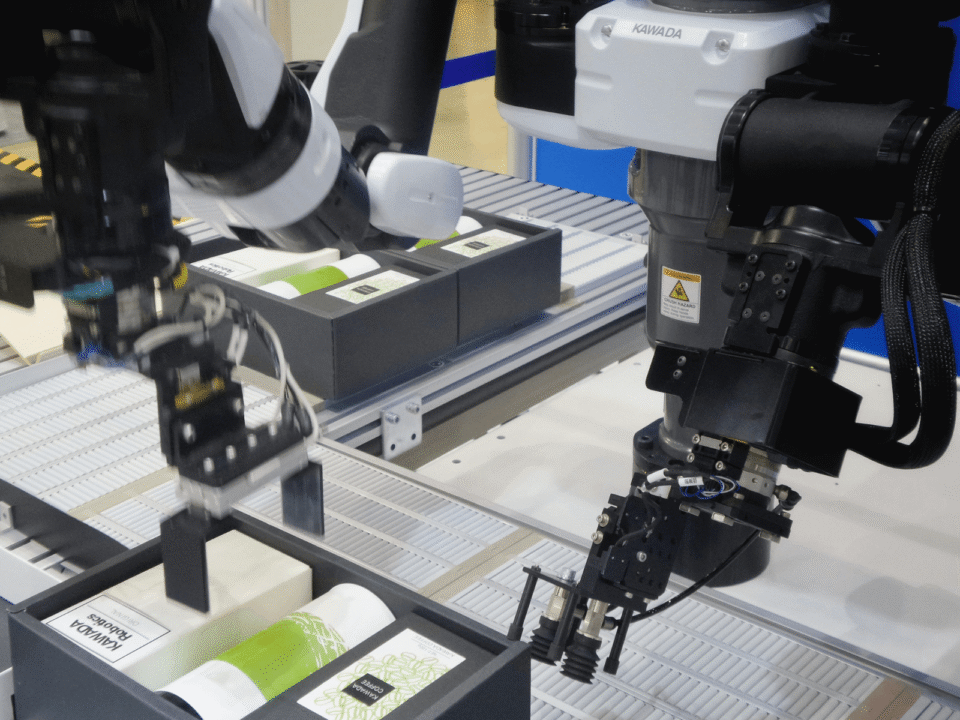 Robotic arms on an automated assembly line picking and placing boxed products, illustrating advanced robotics and precision handling in modern fulfillment operations.