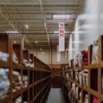Rows of cardboard shelves filled with packaged products in a spacious, orderly warehouse. A red "FLEX" banner hangs from the ceiling, conveying organization.