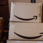 Stacked cardboard boxes with Amazon's smiling arrow logo and yellow tape, conveying a busy delivery or shipping environment.