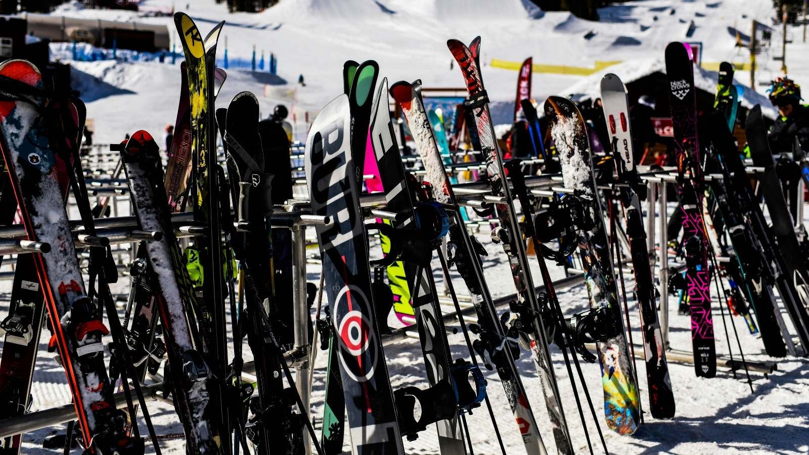 Skis and snowboards arranged in outdoor racks at a snowy winter sports resort, showcasing multiple equipment models and seasonal demand.