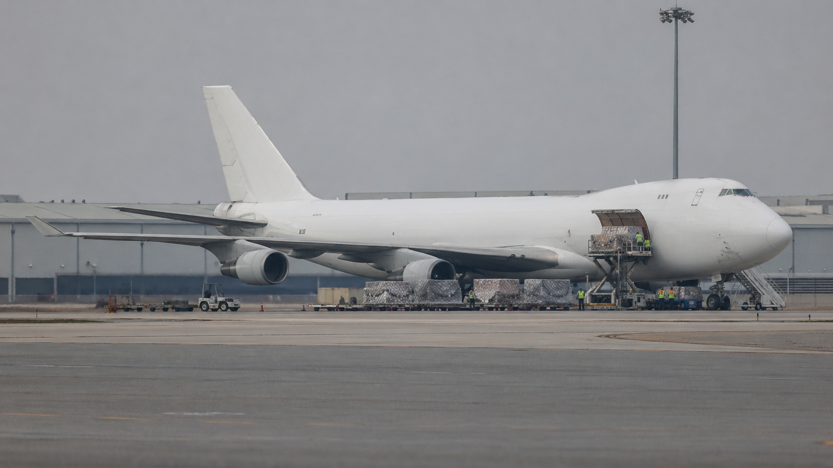 Editorial long-lens photograph of a cargo aircraft on an airport tarmac with freight containers being loaded by ground crew